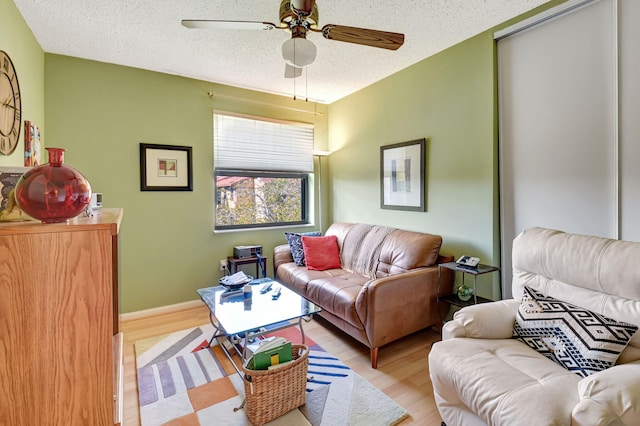 living room featuring ceiling fan, light hardwood / wood-style flooring, and a textured ceiling