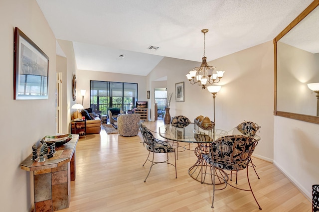 dining space featuring hardwood / wood-style floors, a textured ceiling, vaulted ceiling, and a chandelier