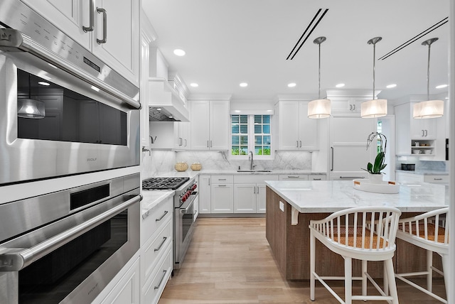 kitchen featuring high end appliances, white cabinets, a sink, and decorative backsplash