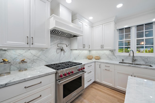 kitchen with light wood-style flooring, luxury stove, a sink, white cabinets, and custom exhaust hood