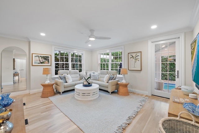 living room with light wood-type flooring, arched walkways, and crown molding