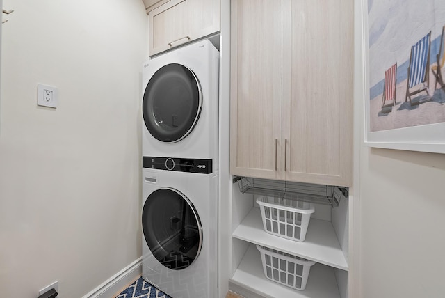 laundry area featuring cabinet space, stacked washer and clothes dryer, and baseboards