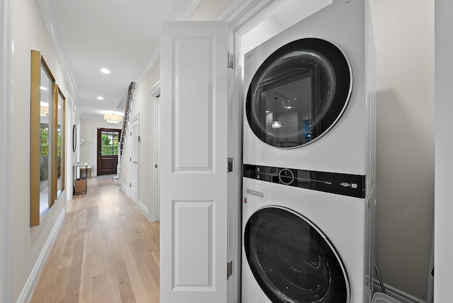 clothes washing area with laundry area, baseboards, light wood-style flooring, ornamental molding, and stacked washing maching and dryer