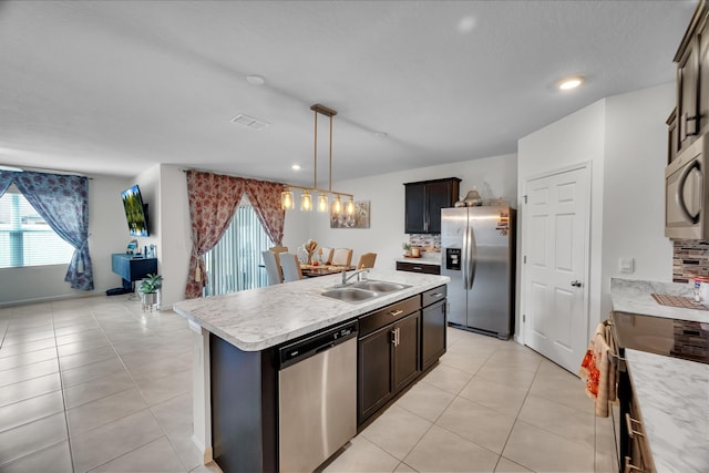 kitchen with appliances with stainless steel finishes, pendant lighting, tasteful backsplash, sink, and a center island with sink