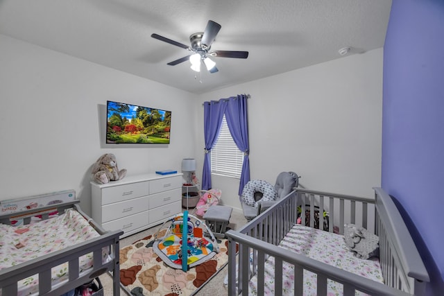 bedroom with a textured ceiling, a crib, and ceiling fan