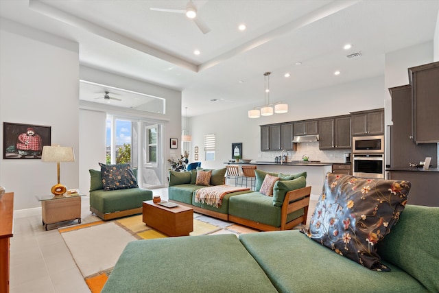 living room featuring sink, a high ceiling, light tile patterned floors, ceiling fan, and a raised ceiling