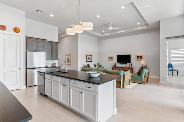 kitchen with stainless steel appliances, an island with sink, a raised ceiling, and sink