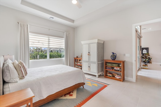 bedroom with a raised ceiling, light tile patterned floors, and ceiling fan