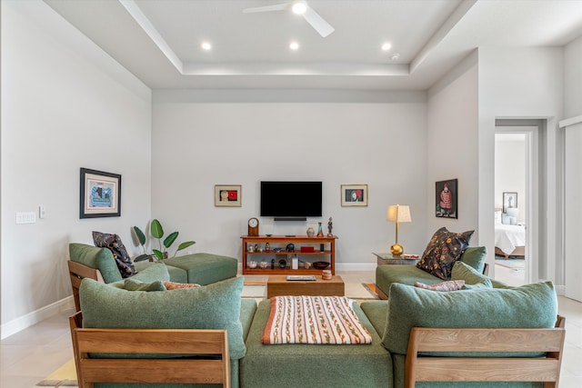 tiled living room with ceiling fan and a tray ceiling