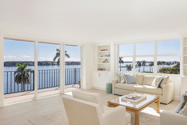 living room with a water view, a wealth of natural light, light hardwood / wood-style floors, and built in shelves