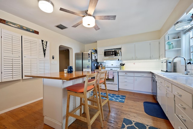 kitchen with white electric range oven, arched walkways, freestanding refrigerator, open shelves, and a sink