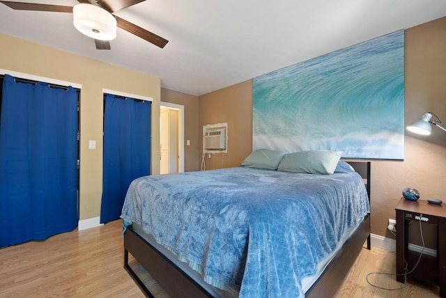 bedroom with baseboards, a wall unit AC, ceiling fan, light wood-type flooring, and multiple closets