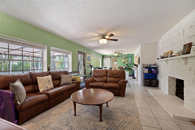 living area with a ceiling fan, light tile patterned flooring, a fireplace, and a textured ceiling