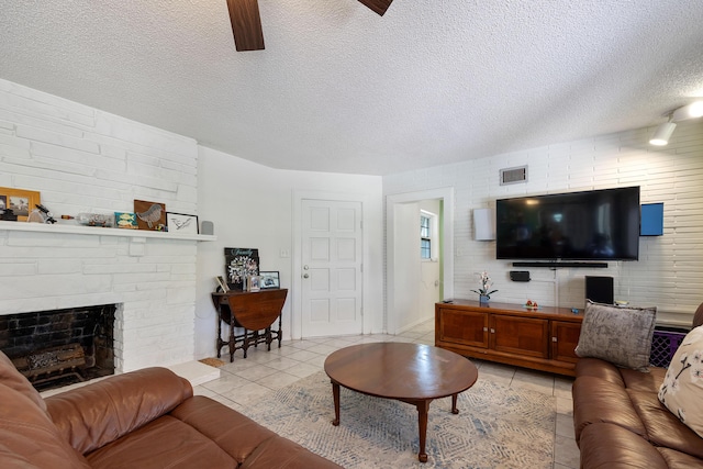 living area featuring a large fireplace, visible vents, a textured ceiling, and light tile patterned floors