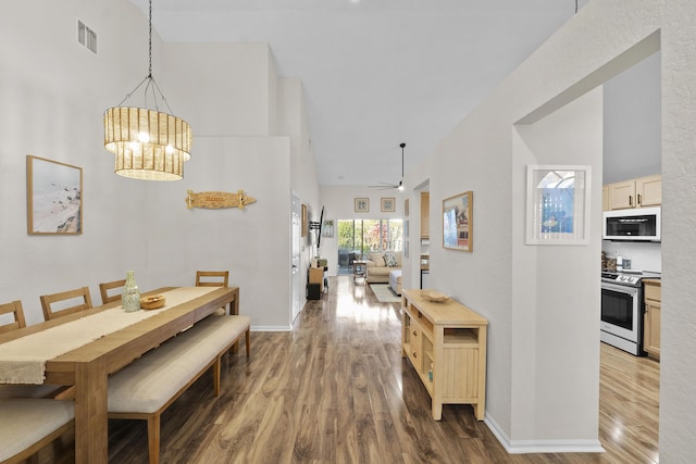 dining space featuring hardwood / wood-style flooring, ceiling fan with notable chandelier, and a high ceiling