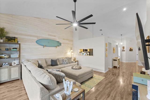 living room with a towering ceiling, light hardwood / wood-style flooring, ceiling fan, and wood walls