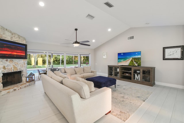 living room featuring lofted ceiling, a stone fireplace, visible vents, and light wood-style floors