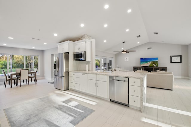 kitchen with light stone counters, stainless steel appliances, a sink, white cabinetry, and open floor plan