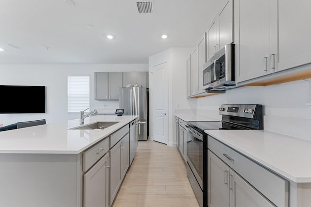 kitchen featuring gray cabinets, appliances with stainless steel finishes, sink, and a kitchen island with sink