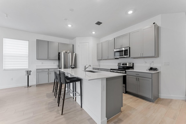 kitchen featuring an island with sink, sink, a breakfast bar area, gray cabinetry, and stainless steel appliances