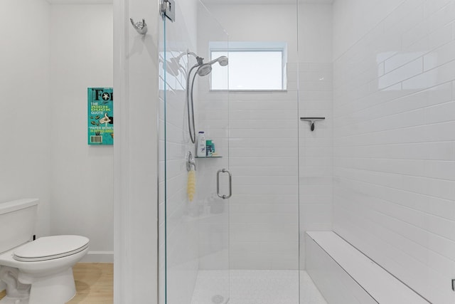 bathroom featuring hardwood / wood-style flooring, a shower with shower door, and toilet