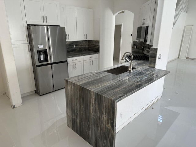 kitchen with sink, stainless steel fridge, white cabinets, dark stone counters, and backsplash