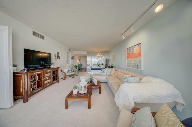 living room with a notable chandelier, track lighting, a textured ceiling, and carpet