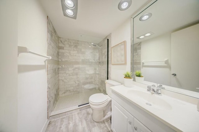 bathroom with hardwood / wood-style floors, vanity, a tile shower, and toilet