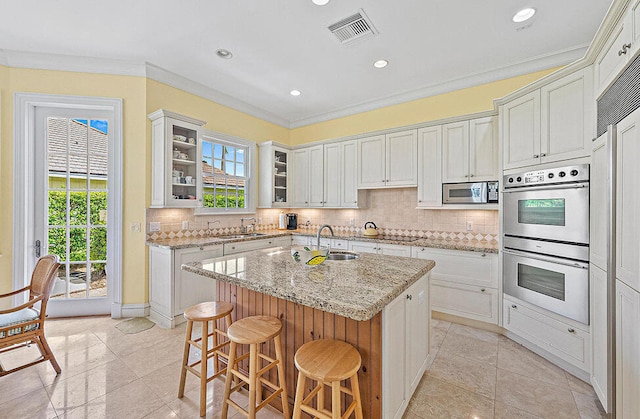 kitchen with appliances with stainless steel finishes, light stone counters, tasteful backsplash, an island with sink, and white cabinets