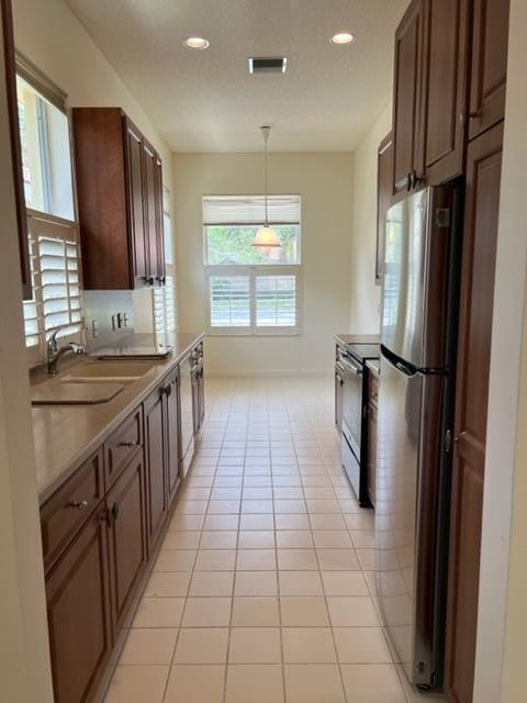 kitchen featuring electric stove, sink, pendant lighting, stainless steel fridge, and light tile patterned flooring