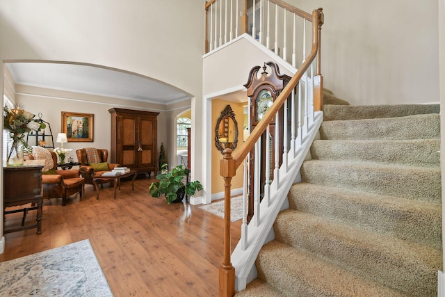 staircase featuring hardwood / wood-style flooring, crown molding, and a towering ceiling