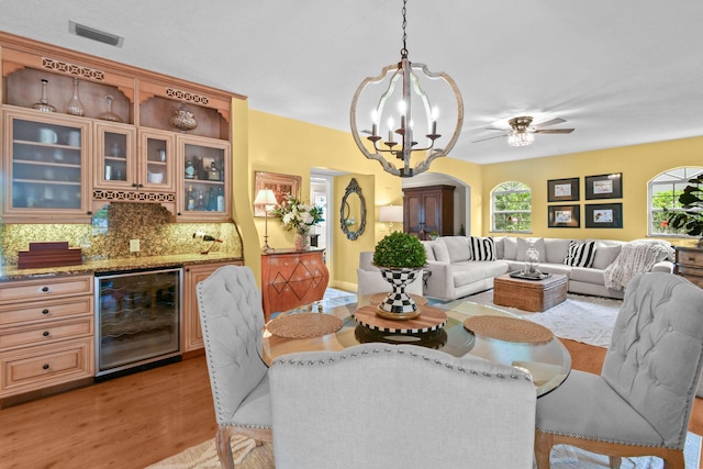 dining area featuring ceiling fan with notable chandelier, bar, light wood-type flooring, and wine cooler