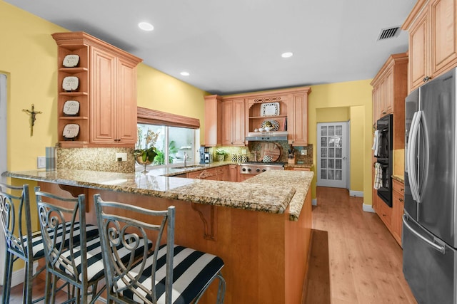 kitchen featuring light stone countertops, decorative backsplash, a breakfast bar, stainless steel refrigerator, and kitchen peninsula