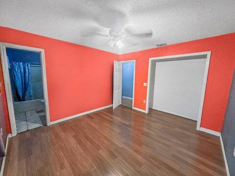 unfurnished bedroom with ceiling fan, a textured ceiling, dark hardwood / wood-style flooring, and ensuite bath