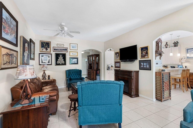 living area with arched walkways, baseboards, light tile patterned floors, and a ceiling fan