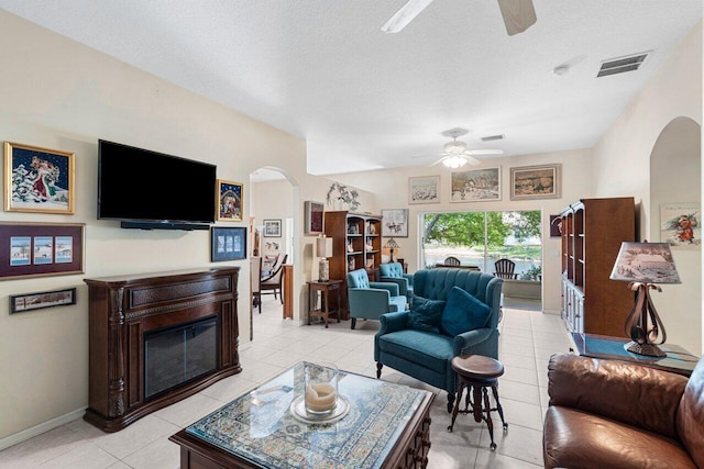living room with visible vents, arched walkways, a ceiling fan, light tile patterned floors, and a glass covered fireplace