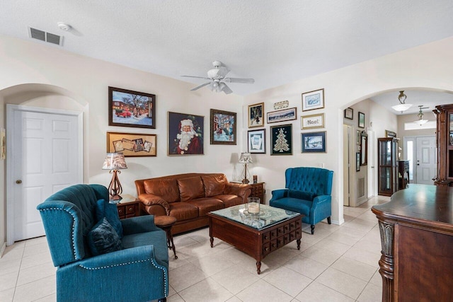 living area featuring light tile patterned floors, visible vents, a ceiling fan, and arched walkways