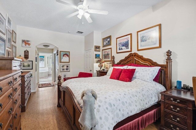 bedroom featuring baseboards, ceiling fan, visible vents, wood finished floors, and arched walkways