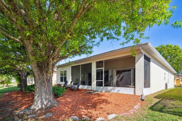 back of house with stucco siding and a sunroom