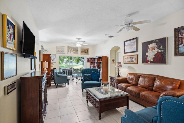 living area with a textured ceiling, arched walkways, a ceiling fan, and light tile patterned floors