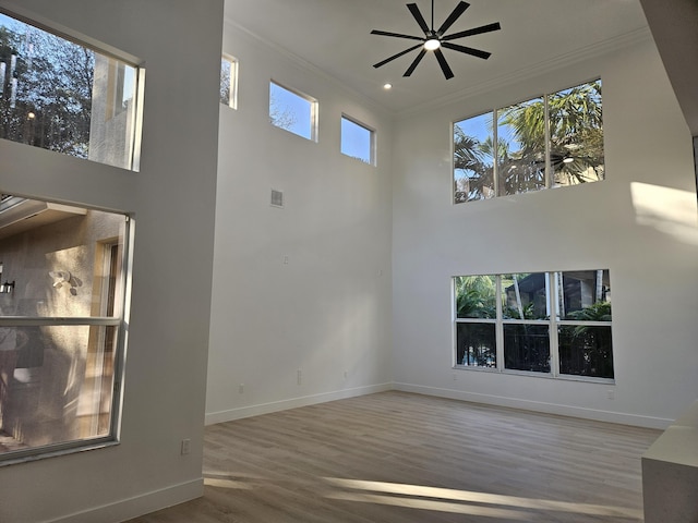 unfurnished living room featuring hardwood / wood-style flooring, crown molding, a towering ceiling, and ceiling fan