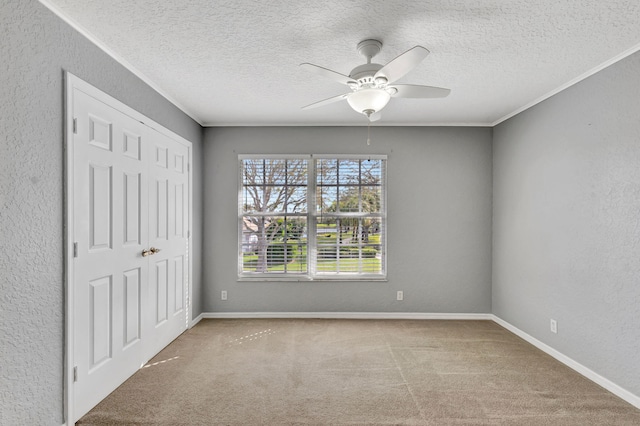 empty room featuring ceiling fan, ornamental molding, light colored carpet, and a textured ceiling