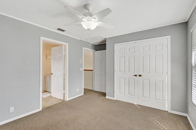 unfurnished bedroom featuring ceiling fan, connected bathroom, a textured ceiling, light colored carpet, and a closet