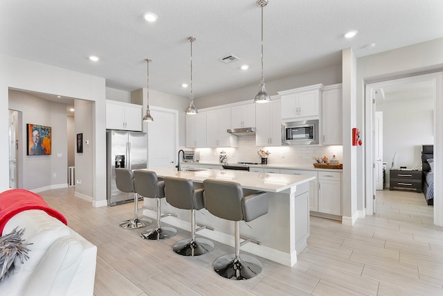 kitchen with stainless steel appliances, white cabinetry, a breakfast bar area, and a center island with sink