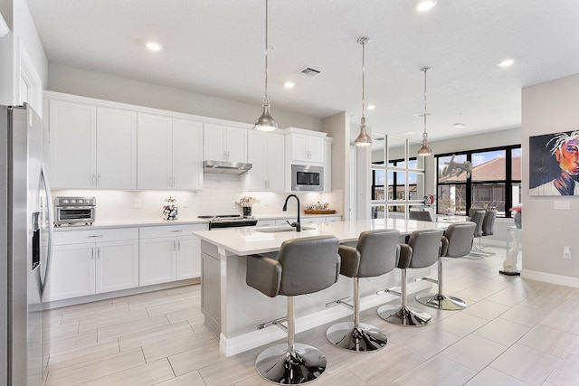 kitchen with sink, a center island with sink, appliances with stainless steel finishes, a kitchen breakfast bar, and pendant lighting