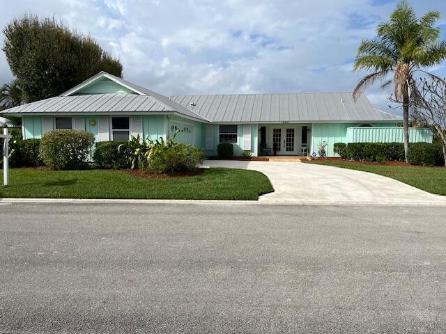 single story home featuring metal roof, an attached garage, concrete driveway, french doors, and a front lawn