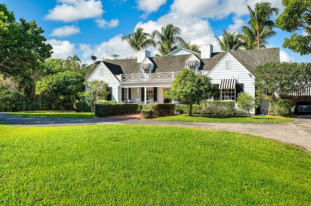 new england style home featuring aphalt driveway, a chimney, a front lawn, and roof with shingles