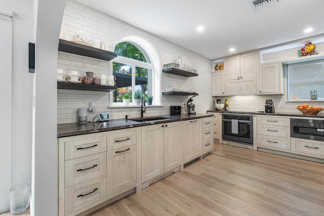 kitchen with sink, light hardwood / wood-style flooring, black oven, oven, and backsplash