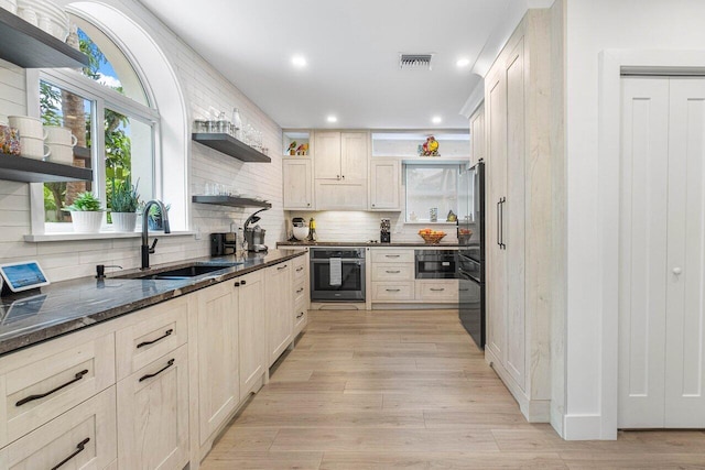 kitchen with sink, backsplash, dark stone counters, stainless steel oven, and light hardwood / wood-style flooring