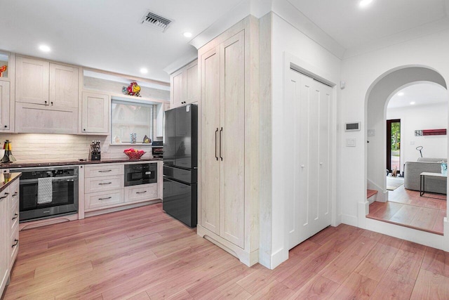 kitchen featuring tasteful backsplash, built in microwave, stainless steel oven, black fridge, and light wood-type flooring